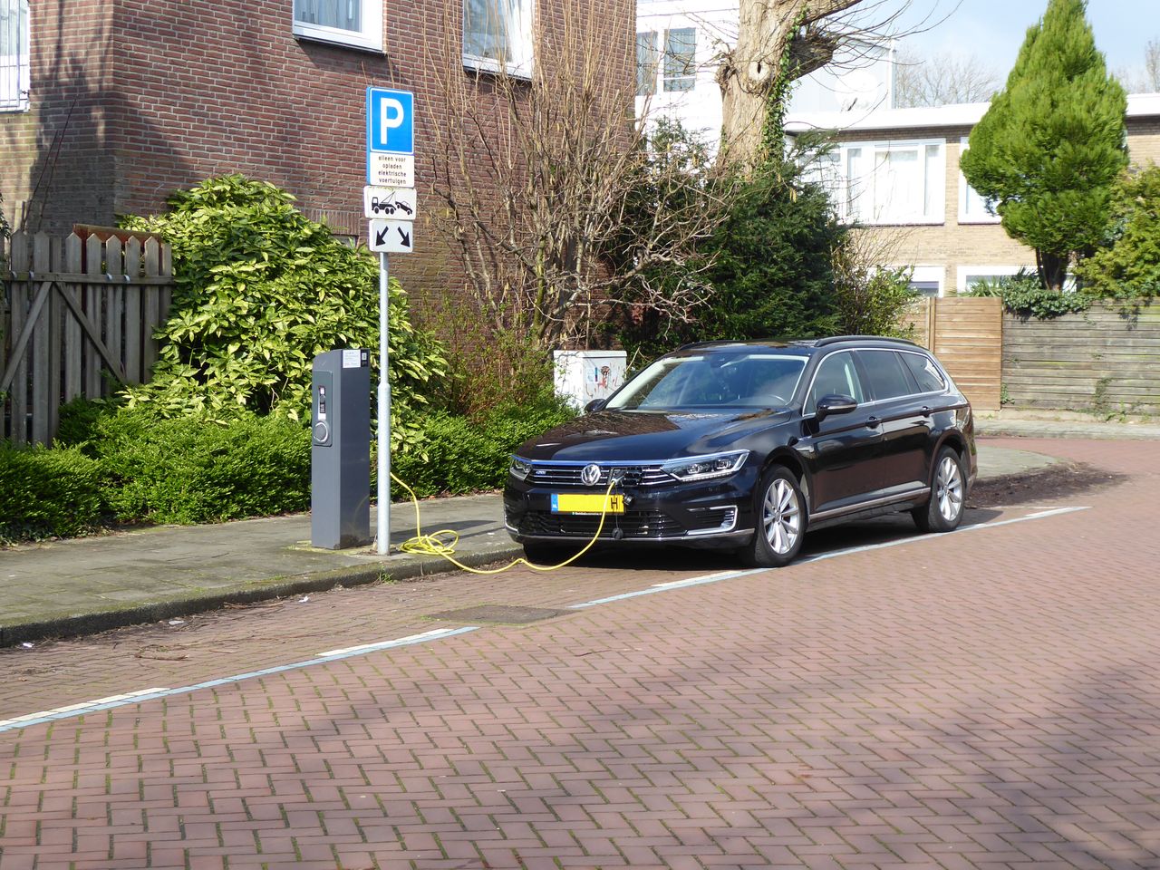 Donkerblauwe elektrische auto aan een openbare laadpaal in een Nederlandse woonstraat