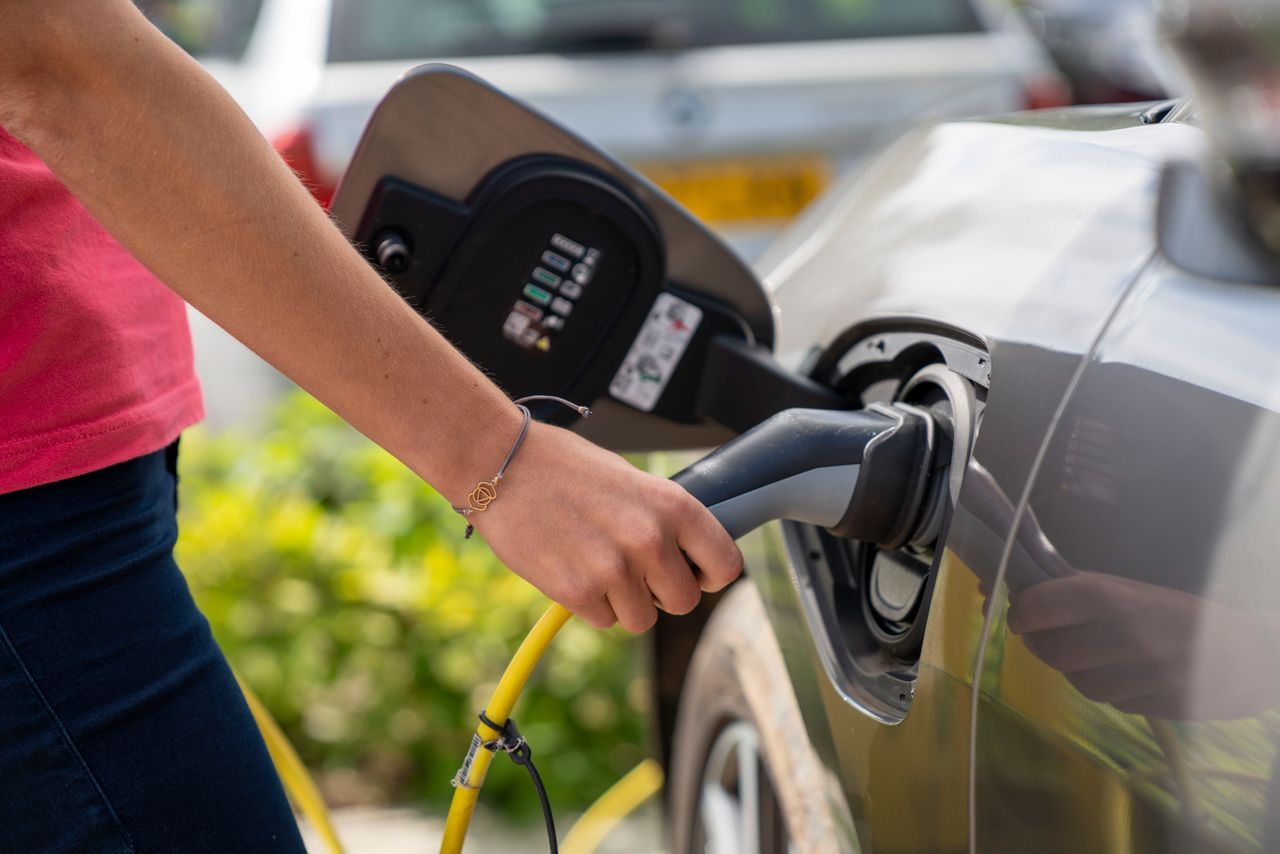 Hand die de laadkabel in een elektrische auto steekt bij een laadpaal buiten