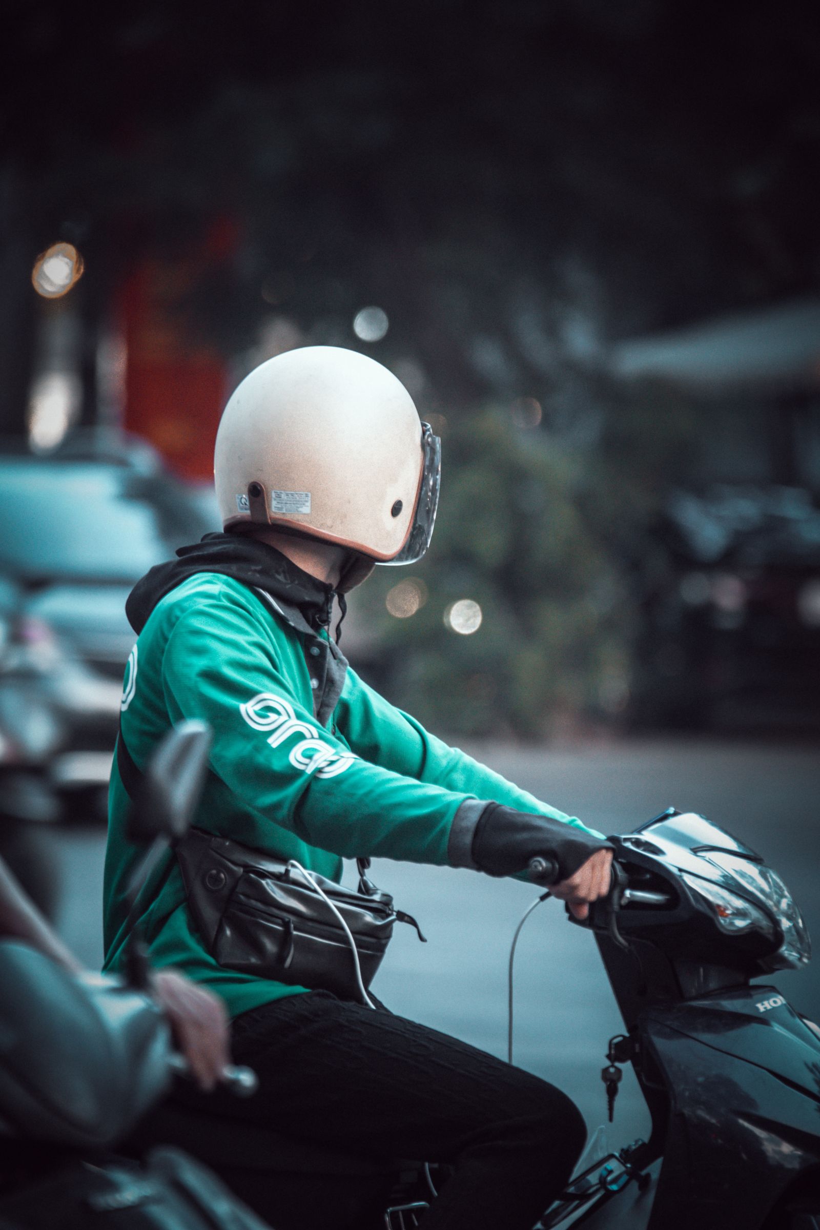 Man met helm rijdt op een motorscooter door de stad, typisch woon-werkverkeer waarbij verbruik telt