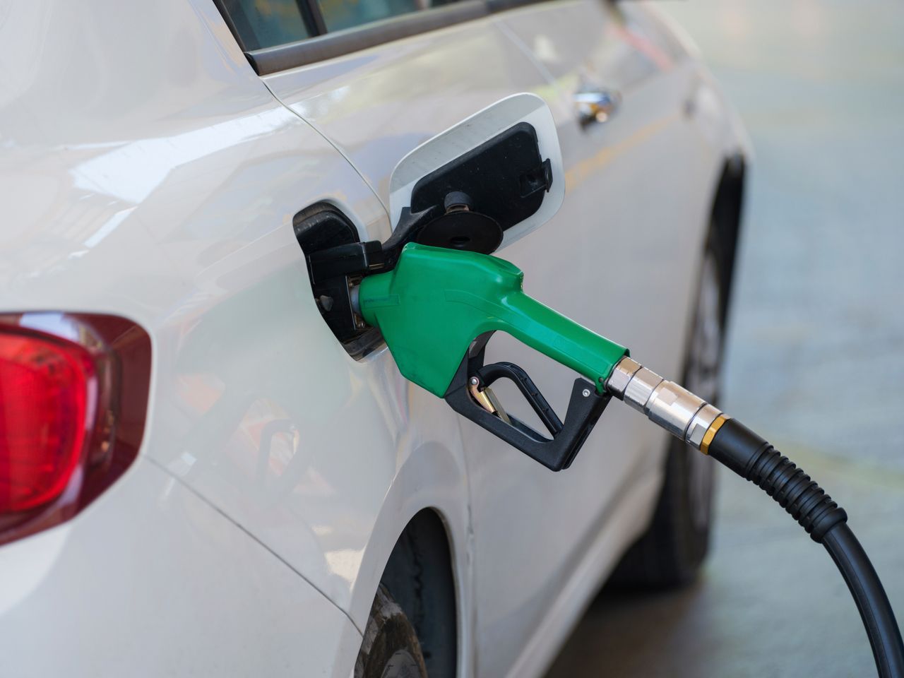 Tankpistool in de tankopening van een witte benzineauto bij een tankstation